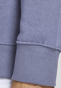 Polsino di felpa lilla con texture a costine e cuciture visibili. Materiale morbido con una finitura liscia.