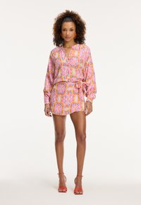 Garais piedurkņu kleita spilgti rozā, oranžā un zilā paisley rakstā; ar saitējamā jostas, apkakles izgriezumu un virs ceļgaliem.