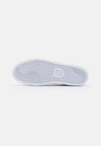 Weiße Sneaker-Sohle mit strukturiertem Gummi für Grip, versehen mit einem Fischgrätenmuster und einem runden Logo im Fersenbereich.