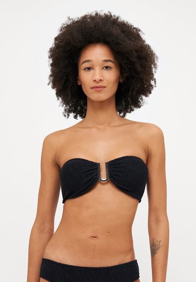 Bikini bandeau noir en tissu texturé, accent en métal en forme de U au centre, et bas assortis. Sans bretelles ni fonctionnalités ajustables.