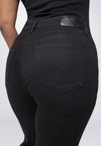 Zwarte denim jeans met een strak ontwerp, voorzien van een enkele achterzak en een leren label met de tekst "FOX FACTOR." Glad textuur, aansluitende pasvorm.