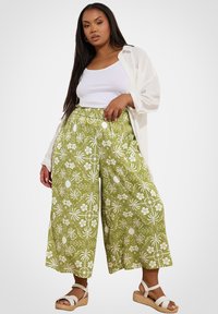 Gröna mönstrade culotter med vita blommönster, elastisk midja och sidofickor, kombinerat med en vit linne och en öppen vit skjorta.