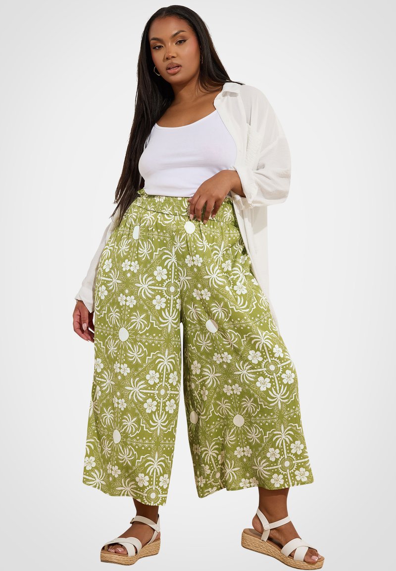 Gröna mönstrade culotter med vita blommönster, elastisk midja och sidofickor, kombinerat med en vit linne och en öppen vit skjorta.
