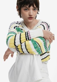 Strickpullover mit horizontalen Streifen in Gelb, Grün, Schwarz und Weiß. V-Ausschnitt-Design mit gerippten Bündchen und Saum.
