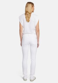 T-shirt bianco in cotone a maniche corte, abbinato a jeans skinny bianchi e sneakers chiare. Vista posteriore, texture liscia, design aderente.