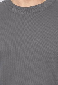 Pull en maille côtelée grise avec un col rond, présentant une surface texturée et un design ajusté, mettant en valeur un motif subtil dans le tissu.