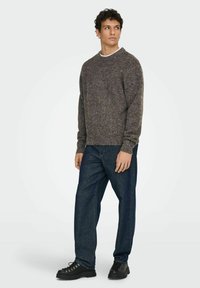 Pull en maille gris avec col rond, manches longues et finition texturée. Associé à un jean en denim bleu et des chaussures noires à lacets.