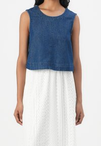 Denim croppad linne med rund halsringning och axelsömmar, i kombination med en strukturerad vit mönstrad kjol.