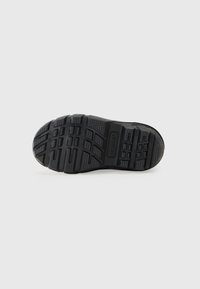 Suela de zapato de goma negra con un patrón de relieve texturizado, que presenta agarres y el nombre de la marca "SOREL" grabado en la superficie.