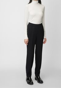 Crème coltrui en zwarte broek met een elastische tailleband. De broek heeft een recht model en een gladde textuur. Zwarte schoenen inbegrepen.