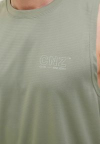 T-shirt de sport sans manches vert en tissu texturé. Il présente un col rond avec le logo "CNZ™" imprimé en blanc.
