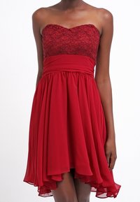 Robe rouge sans bretelles avec un corsage en dentelle, une taille cintrée et une jupe fluide à ourlet asymétrique et texture douce.