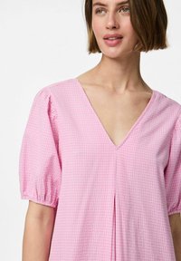 Ružičasta gingham bluzica s dubokim V-izrezom, naboranim kratkim rukavima i detaljem nabora na prednjem dijelu. Napravljen od lagane tkanine.