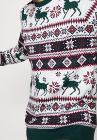 Pull en tricot avec une base blanche ornée de rennes verts, de motifs géométriques rouges et verts, et un ourlet côtelé vert.