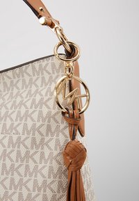 Sac à main Michael Kors beige et marron avec motif répétitif du logo "MK", breloque dorée "MK", poignée en cuir fauve et pampille décorative en cuir.