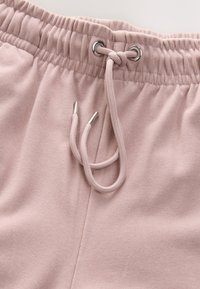 Gros plan sur une ceinture élastique rose pâle avec un cordon de serrage noué et des oeillets en métal sur un pantalon en tissu doux.