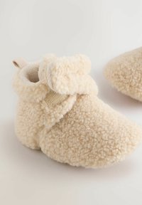 Bottes pour tout-petits beiges fabriquées en tissu texturé et moelleux, avec une forme douce et arrondie. Équipées d'une sangle Velcro et d'une boucle pour un enfilage facile.