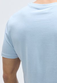 Φωτεινό γαλάζιο κοντομ άνικο μπλουζάκι από απαλό βαμβακερό ύφασμα, με στρογγυλή λαιμόκοψη και λεία υφή. Εμφανίζει την πίσω όψη.