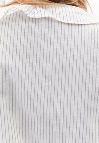 Weiße gestreifte Bluse mit einem weichen Kragen. Verfügt über vertikale dunkle Streifen auf leichtem Stoff und präsentiert ein entspanntes und sauberes Design.