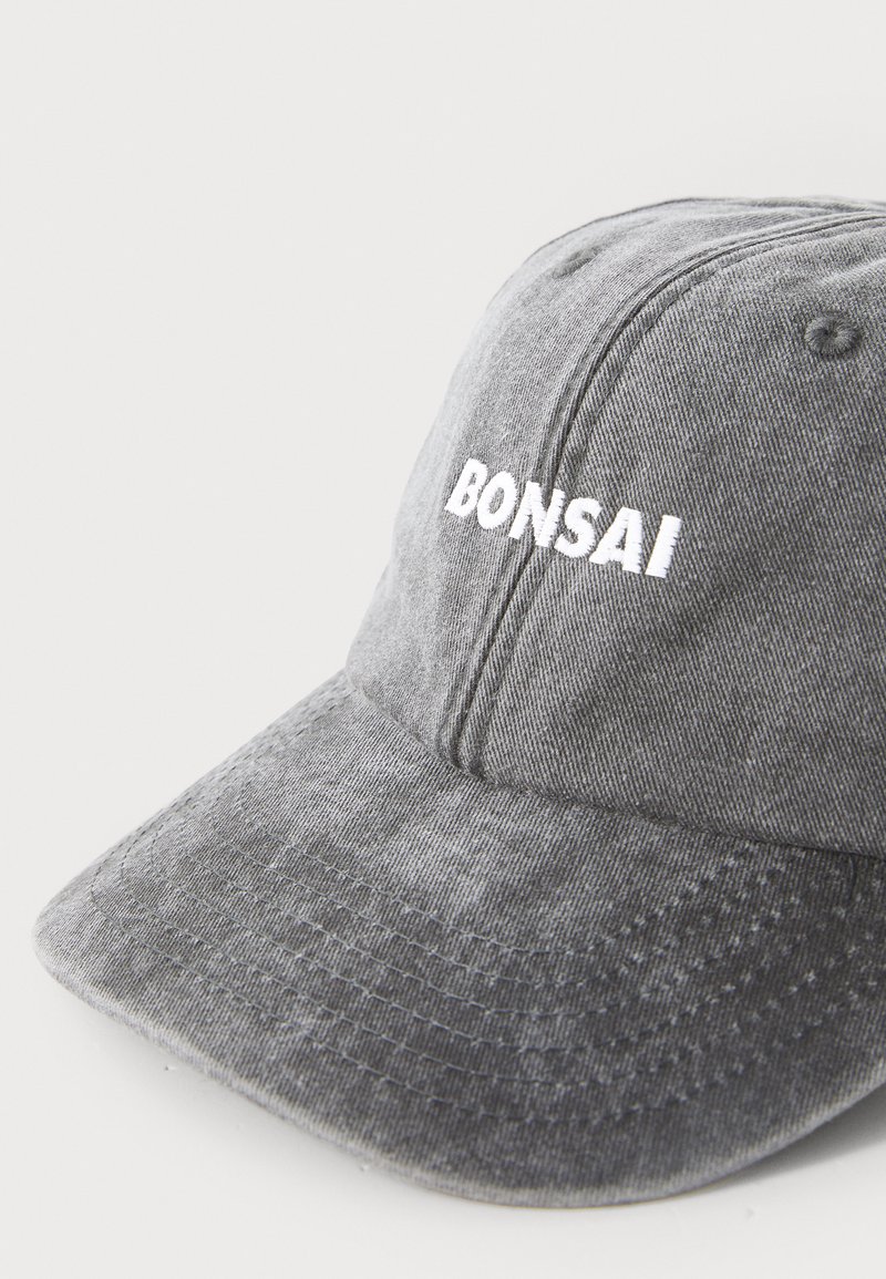 Grå bomuldske med en buet skygge, der har hvid broderet tekst "BONSAI" på fronten. Blød tekstur med synlige syningsdetaljer.