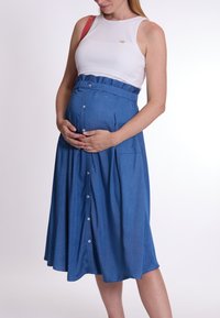Jupe en denim bleu moyen avec des boutons, dotée d'une taille froncée et de deux poches latérales. Associée à un haut sans manches blanc.