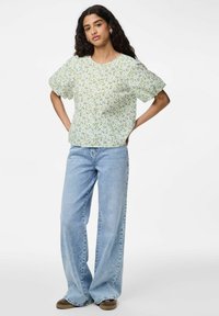 Blomstret kortærmet bluse i lys grøn, mønstret med små blomster. Kombineret med lyseblå vide jeans og brune sko.