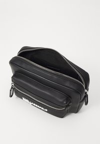 Schwarze Ledertasche mit zwei Reißverschlussfächern, strukturierten Oberflächen, silbernen Beschlägen und einem Logodetail auf der Vorderseite.