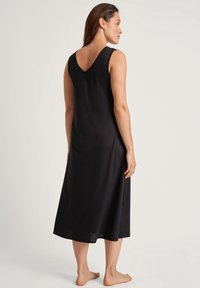 Abito nero senza maniche con scollatura a V sul retro, silhouette morbida, realizzato in materiale soffice, lunghezza al ginocchio, taglio su misura.