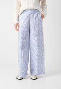 Pantalons larges bleu clair avec un motif abstrait crème, dotés de poches latérales et d'une taille élastique, associés à un pull crème.