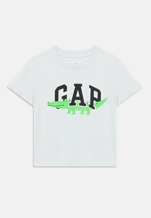 T-shirt blanc à manches courtes pour enfants avec le texte "GAP" en noir et un crocodile cartoon vert intégré aux lettres à l'avant.