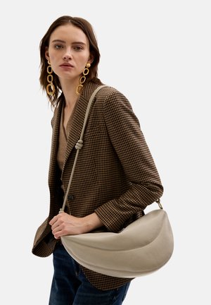 Beige læder skuldertaske med en halvmåneform, glat tekstur og diskrete syninger. Båret sammen med en brun houndstooth-blazer og denim.