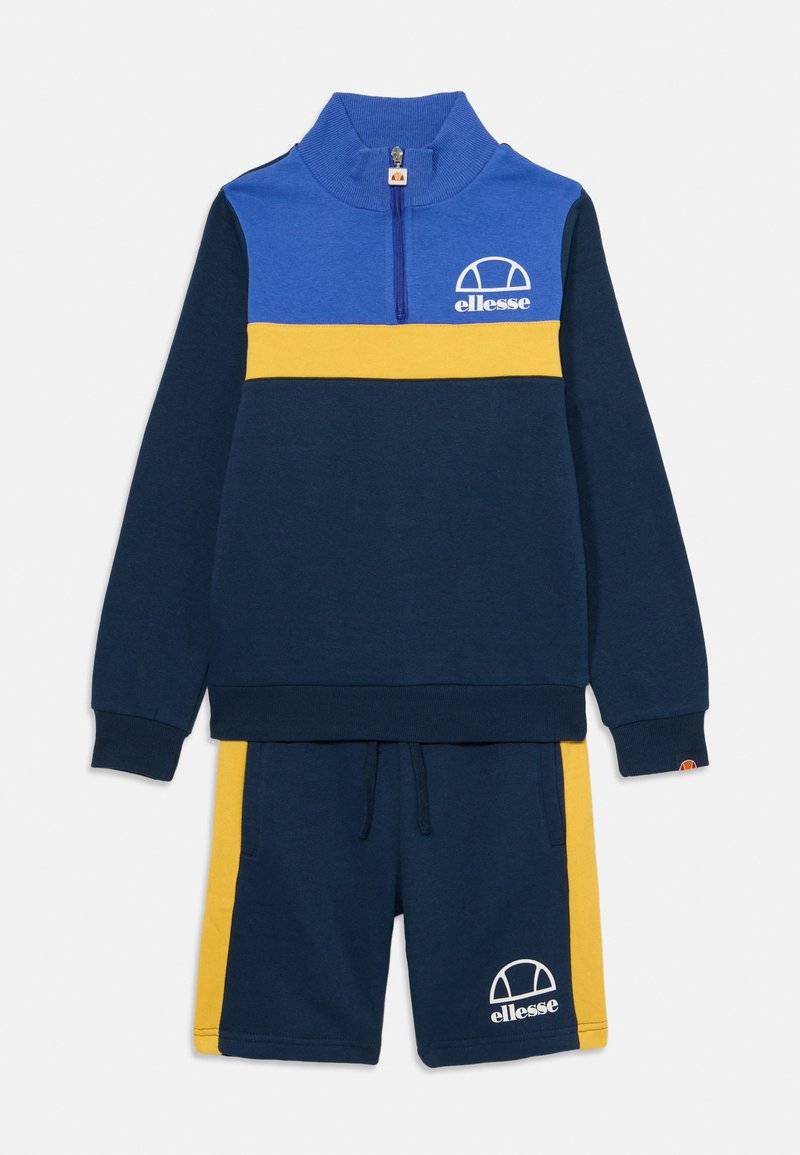 Marineblauer Trainingsanzug bestehend aus einem Reißverschluss-Oberteil mit einem blauen und gelben Streifen sowie passenden Shorts mit einem gelben Seitenpanel und Logo.