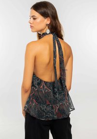 Top halter de color negro y rojo con estampado, con la espalda descubierta y un dobladillo con volantes, fabricado en un tejido ligero. Presenta un cierre de cuello atado.