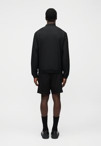 Melna bomber jakas ar teksturētu apdari, kombinēta ar melnām šortiem. Apģērbs ir ar piegulošu vidukli un minimālistiskiem dizaina elementiem.