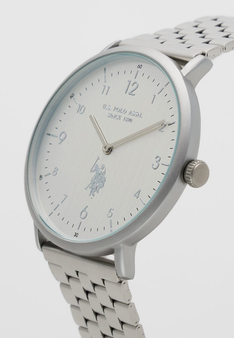 Orologio analogico argento con quadrante in metallo spazzolato, dettagli in aqua e cinturino in rete. Presenta un logo e indici orari in numeri arabi.