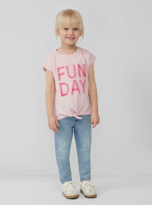 Hellblaues T-Shirt mit "FUN DAY" in flauschigen pinken Buchstaben, am Saum geknotet, kombiniert mit hellblauen Jeans und weißen Sneakern.