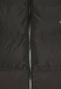 Giacca a vento nera con un esterno liscio e lucido e una zip a lunghezza totale. Caratterizzata da una sezione inferiore testurizzata e da un logo discreto.