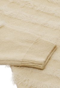 Maglione color crema con una finitura morbida e testurizzata. Presenta polsini a coste e un design morbido, leggermente sfilacciato.