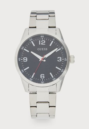 Hõbedane metallist randmevaat, musta taustaga, valged tundemärgid, kolm käe, mis näitavad kellaaega 10:08:35, ja "GUESS" logo 12-kiire all.