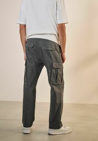 Pantalones cargo grises con múltiples bolsillos laterales, un ajuste relajado y un diseño sencillo. Combinados con una camiseta blanca casual y zapatillas blancas.