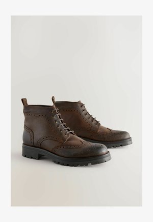 Braune Leder-Stiefeletten mit Broguemuster, runder Spitze und schwarzen Gummisohlen. Mit Schnürverschluss und einer Zuglasche an der Rückseite.