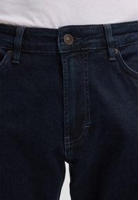 Jeans in denim blu scuro con taglio dritto, dotati di chiusura con zip, tasche frontali e dettagli di cucitura a contrasto lungo le cuciture.
