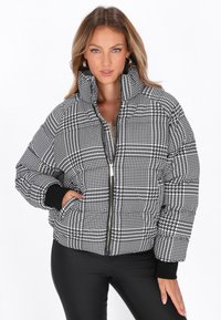 Giacca puffer a scacchi bianco e nero con collo alto, chiusura con zip e polsini a coste. Presenta un materiale testurizzato con un motivo audace.
