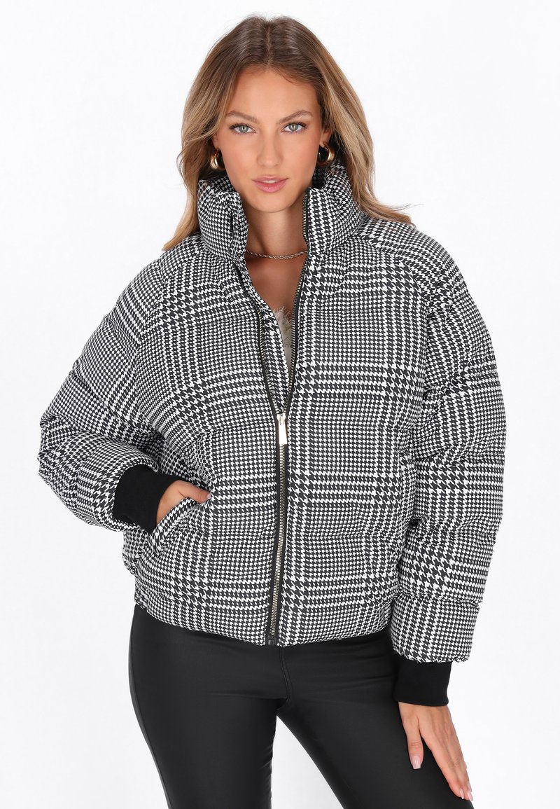 Giacca puffer a scacchi bianco e nero con collo alto, chiusura con zip e polsini a coste. Presenta un materiale testurizzato con un motivo audace.