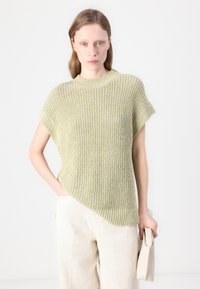 Suéter de punto en amarillo claro y gris con un patrón texturizado, mangas cortas y un dobladillo asimétrico, combinado con pantalones de pierna ancha beige.