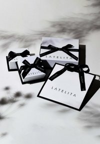 Fyra vita presentlådor med svart band som har varumärket "LATELITA", som varierar i storlek, med en stilren rektangulär form och skarpa kanter.