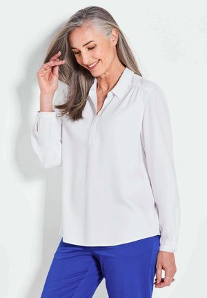 Weißes Langarmhemd mit Kragen, in entspannter Passform und subtiler Glanz, getragen mit blauen Hosen. Glatte Textur und einfaches Design.