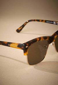 Sunglasses od kornjačevine s smeškom staklima i elegantnim okvirom. 'SIGNATURE' ugravirano na kraku. Prozirni nosači za nos.