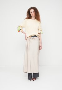 Pull en maille crème avec broderies florales sur les manches, associé à une jupe beige drapée et un pantalon large gris, complété par des sandales noires.