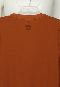 Nike Dri-FIT t-shirt i bränd orange, tillverkad av texturerat tyg med rund hals och etikettinformation nära axeln.